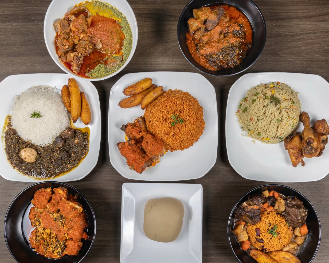 Assorted M&M plates with jollof, fried rice, soup, plantain, and proteins arranged across the table